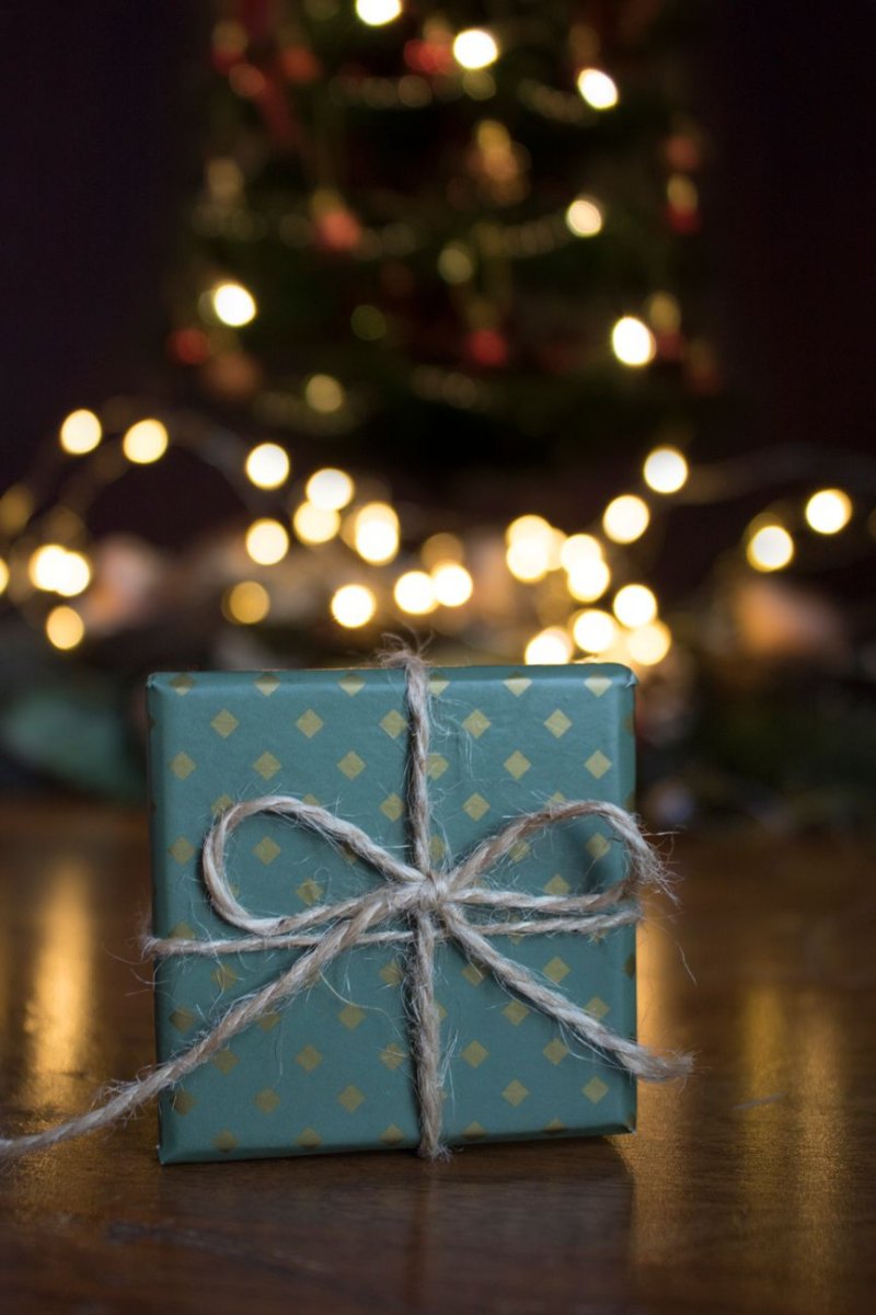 Liten turkos ask med guldmönster knuten med snöre framför suddiga ljus och julgran