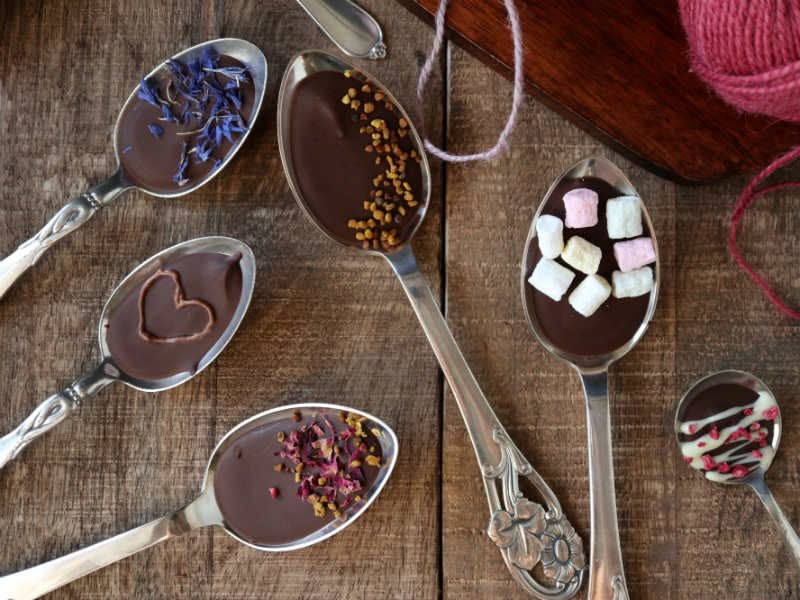 Silverskedar doppade i mörk choklad med blåklint, chokladhjärta, bipollen, rosenblad, marshmallows och vit chokladdekor