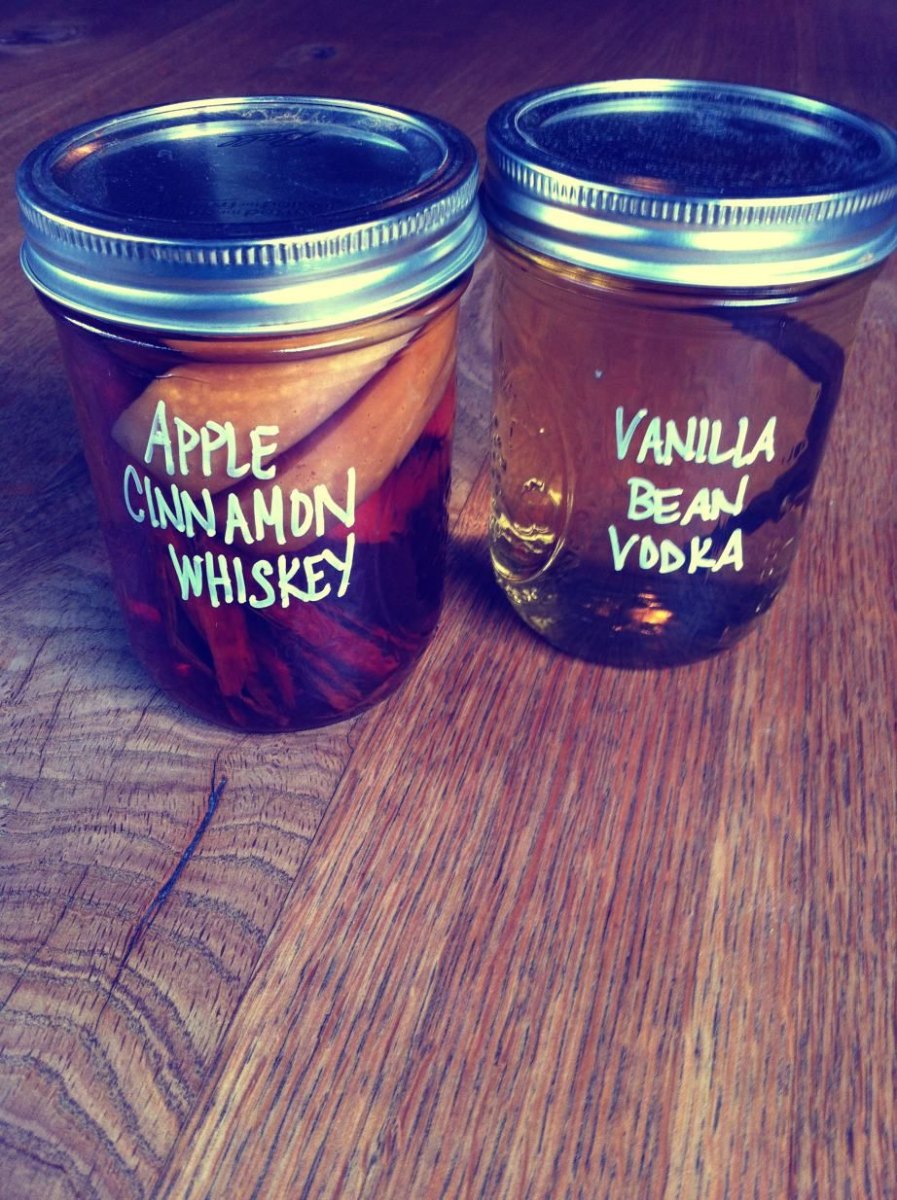 Två glasburkar med smaksatt sprit och handskrivna etiketter: äpple och kanel i whiskey, vaniljstång i vodka